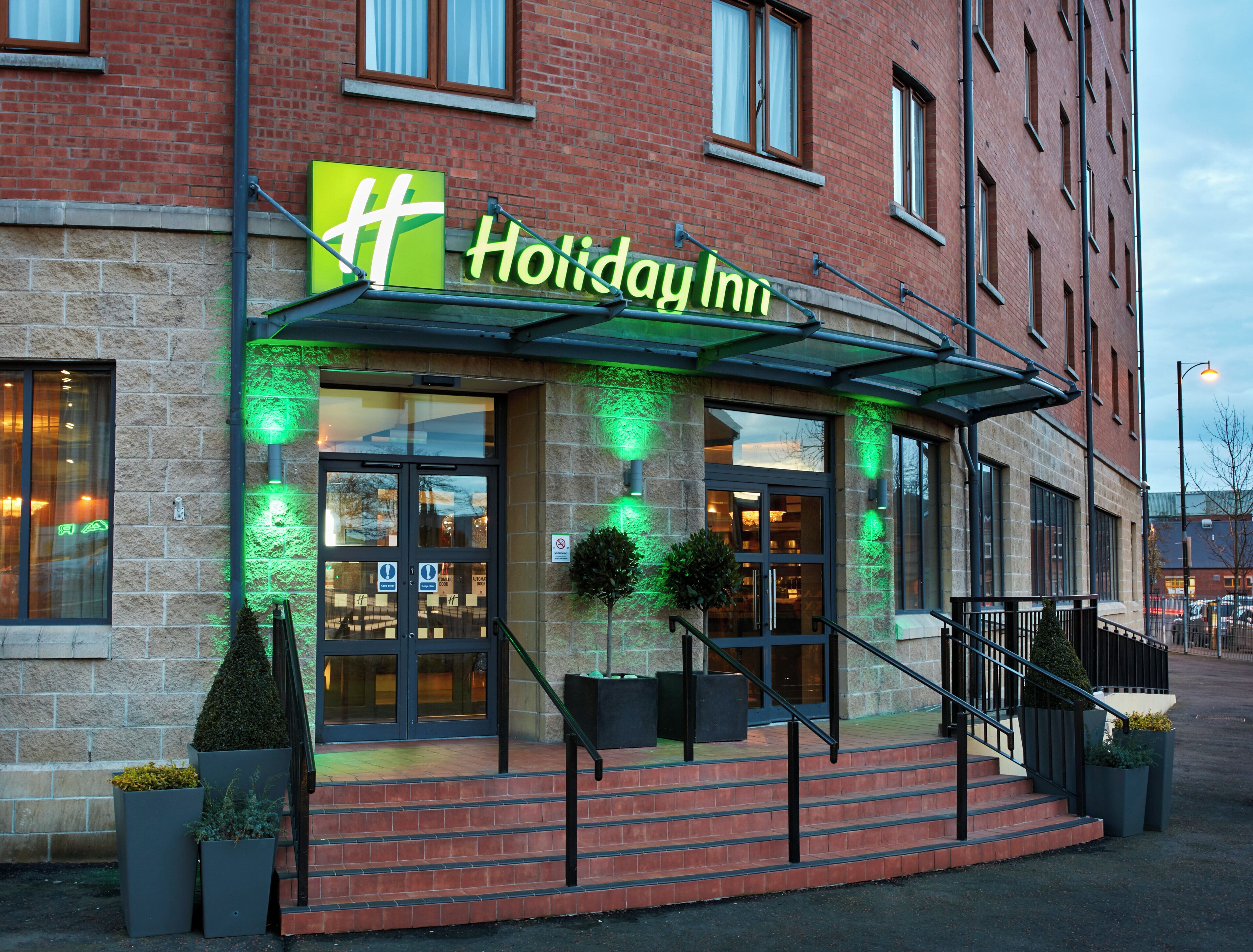 L’entrée d’un hôtel Holiday Inn, avec un auvent en verre, une façade en briques et un escalier menant à l’entrée.