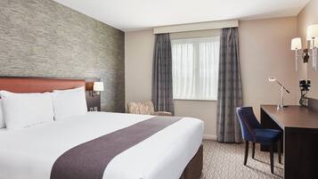 Una habitación de hotel con una cama grande, un escritorio, una silla, una lámpara y una ventana con cortinas.