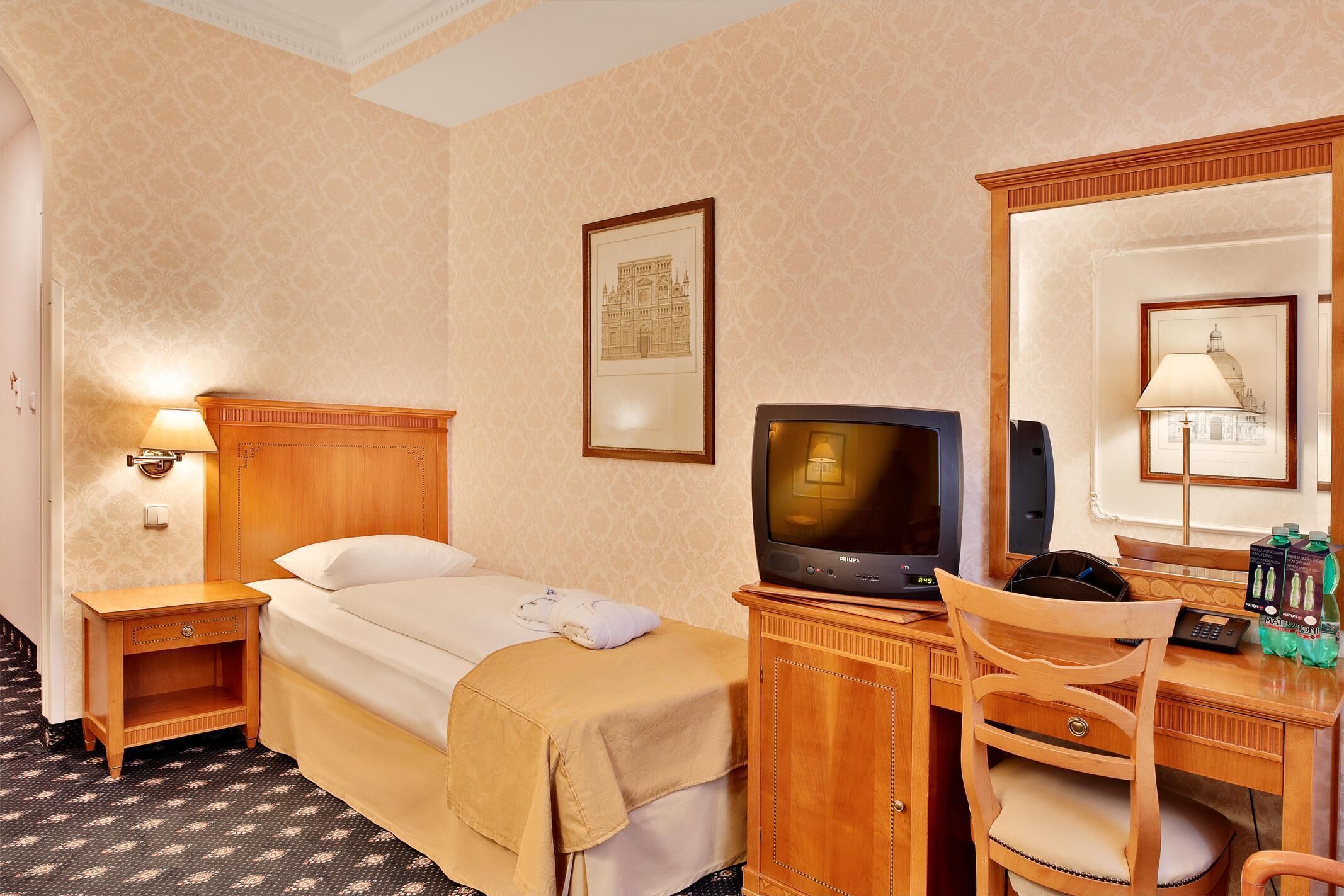 A hotel room with a bed, a desk with a computer, a chair, a television, and a mirror.