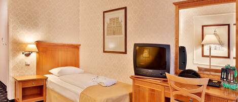 A hotel room with a bed, a desk with a computer, a chair, a television, and a mirror.