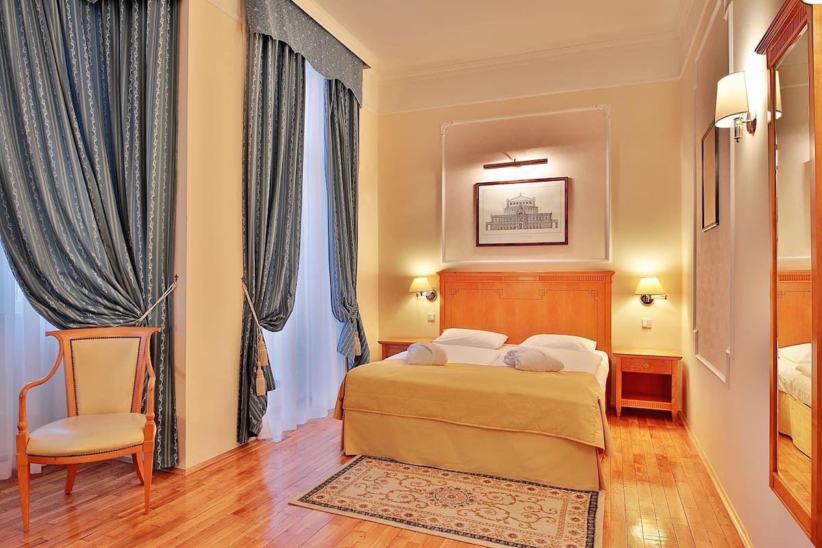 A hotel room with a bed, a chair, a nightstand, a lamp, and a framed picture on the wall.