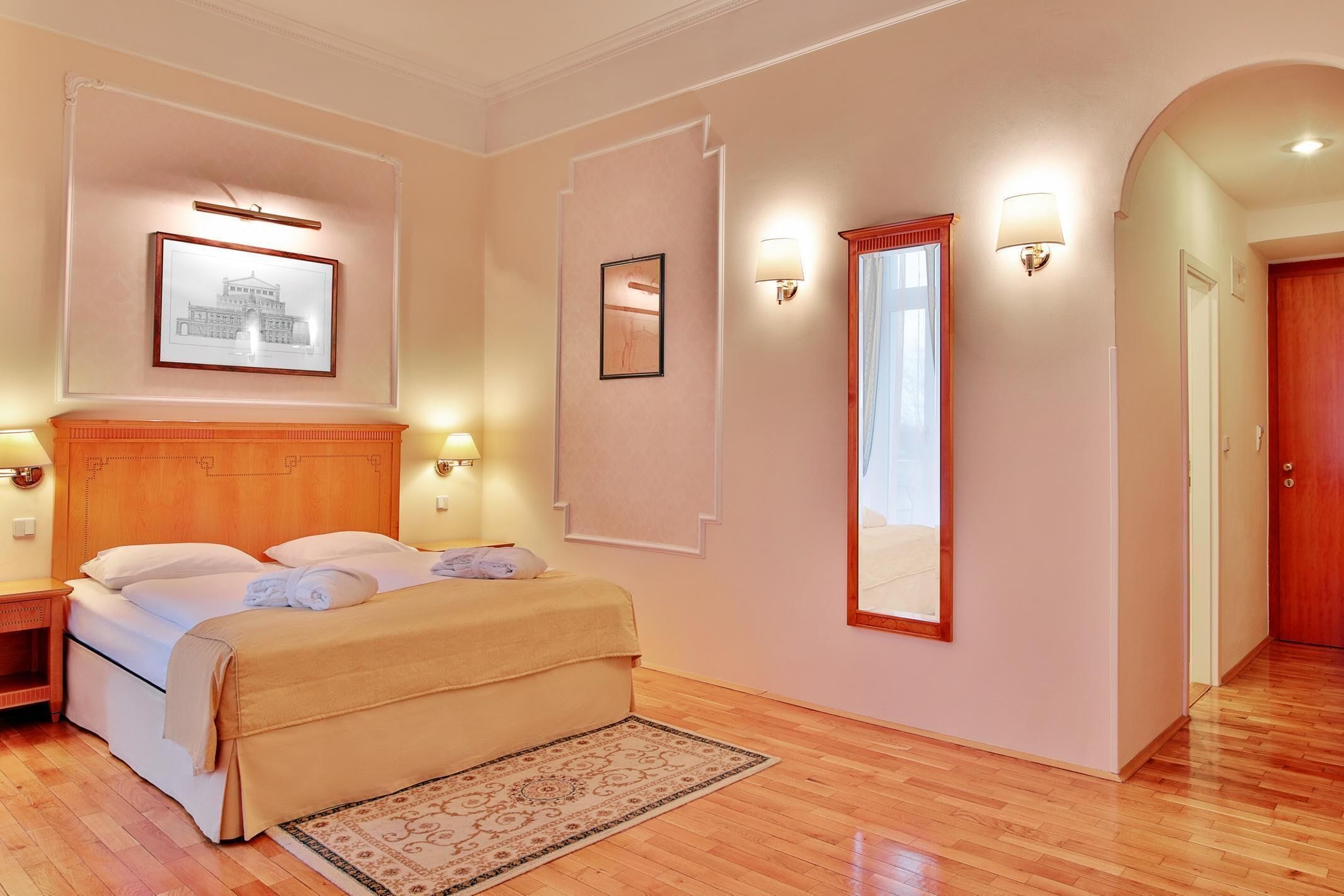 Una habitación de hotel con una cama de madera, un espejo grande y cuadros en las paredes.