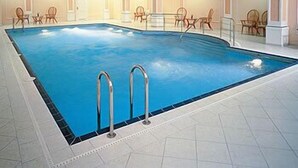 An indoor swimming pool with clear water, surrounded by chairs and a tiled floor. - Parkhotel Richmond (Karlovy Vary)