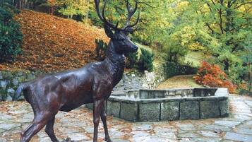 A deer statue in a garden setting with stone pathways and autumn foliage.