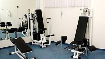 Academia com diversos equipamentos de exercício, incluindo um banco, máquinas de peso e um remo.