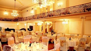 A banquet hall with round tables, chairs with white covers, chandeliers, and a balcony with ornate railings. - Parkhotel Richmond (Karlovy Vary)