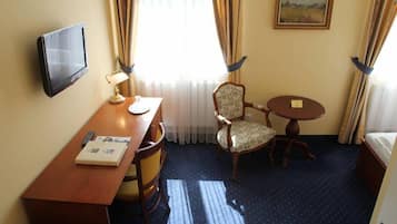 Ett hotellrum med ett skrivbord, en stol, ett nattduksbord, en lampa och en tv som är monterad på väggen.