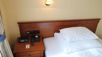 A hotel room with a wooden headboard, a bedside table with a telephone and a notepad, and a bed with white linens.