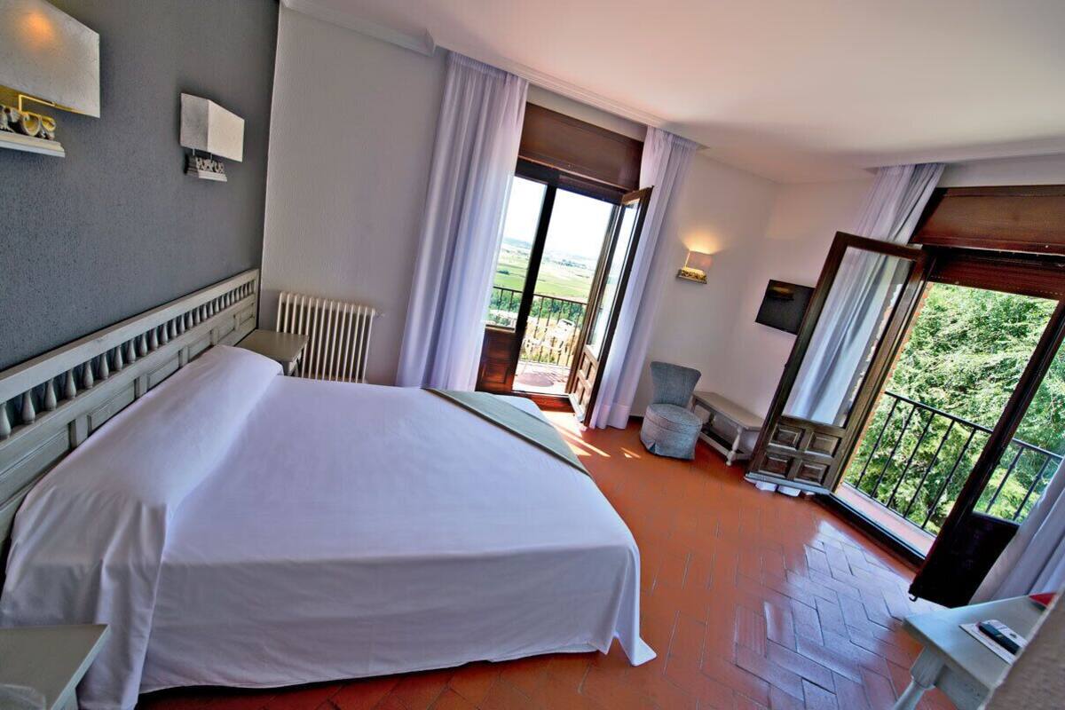 A hotel room with a large bed, a view of the outdoors, a balcony, and a chair.