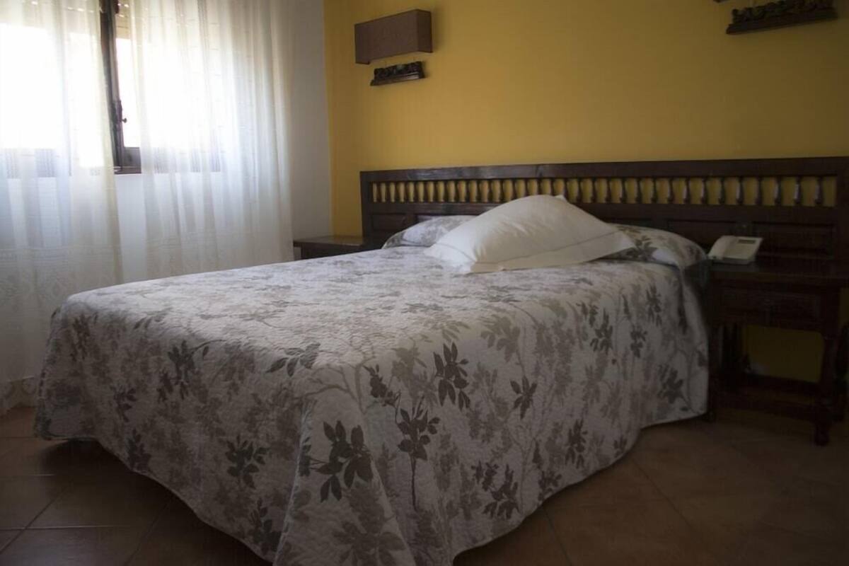 A bed with a floral bedspread, a bedside table with a lamp, and a wall-mounted telephone.