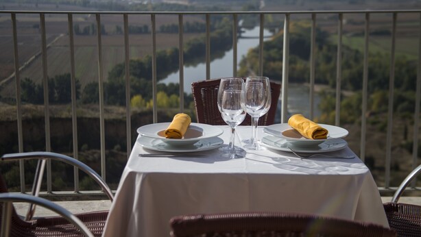 A table set for two with plates, glasses, and a napkin, overlooking a scenic landscape with a river and fields. - Hospedium Hotel Juan II (Toro)