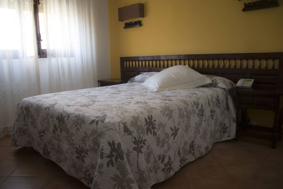 A bed with a floral bedspread, a nightstand with a phone, and a wall-mounted shelf.