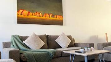 Uma sala de estar com um sofá, duas almofadas, uma mesa de centro e um quadro na parede.