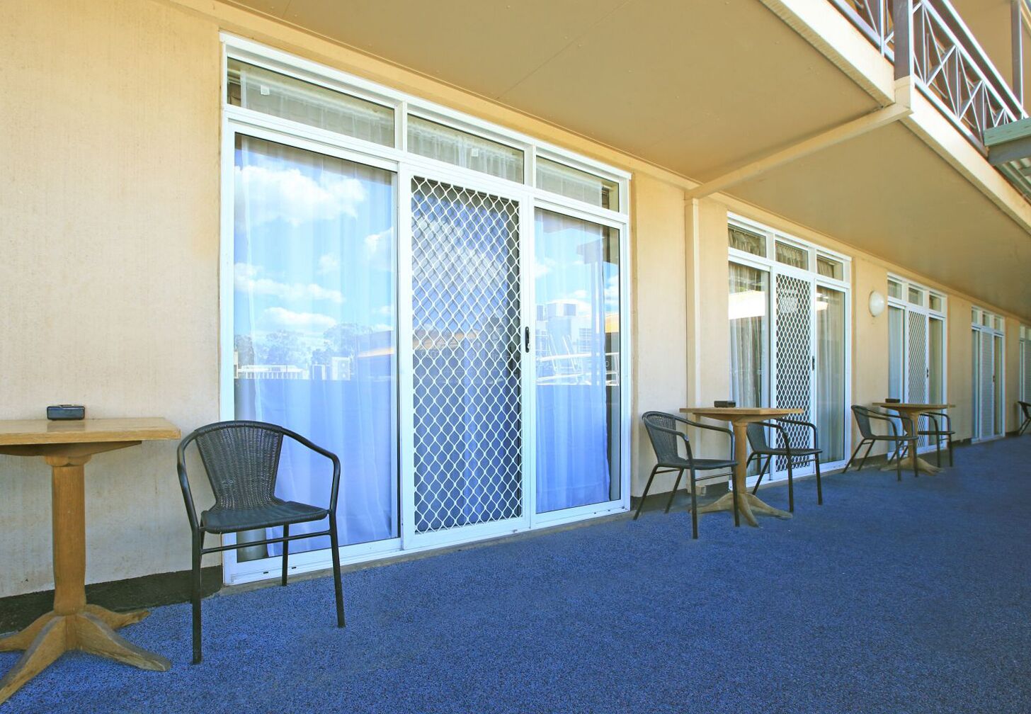 A corridor with sliding glass doors, a blue carpet, and outdoor seating with tables and chairs.