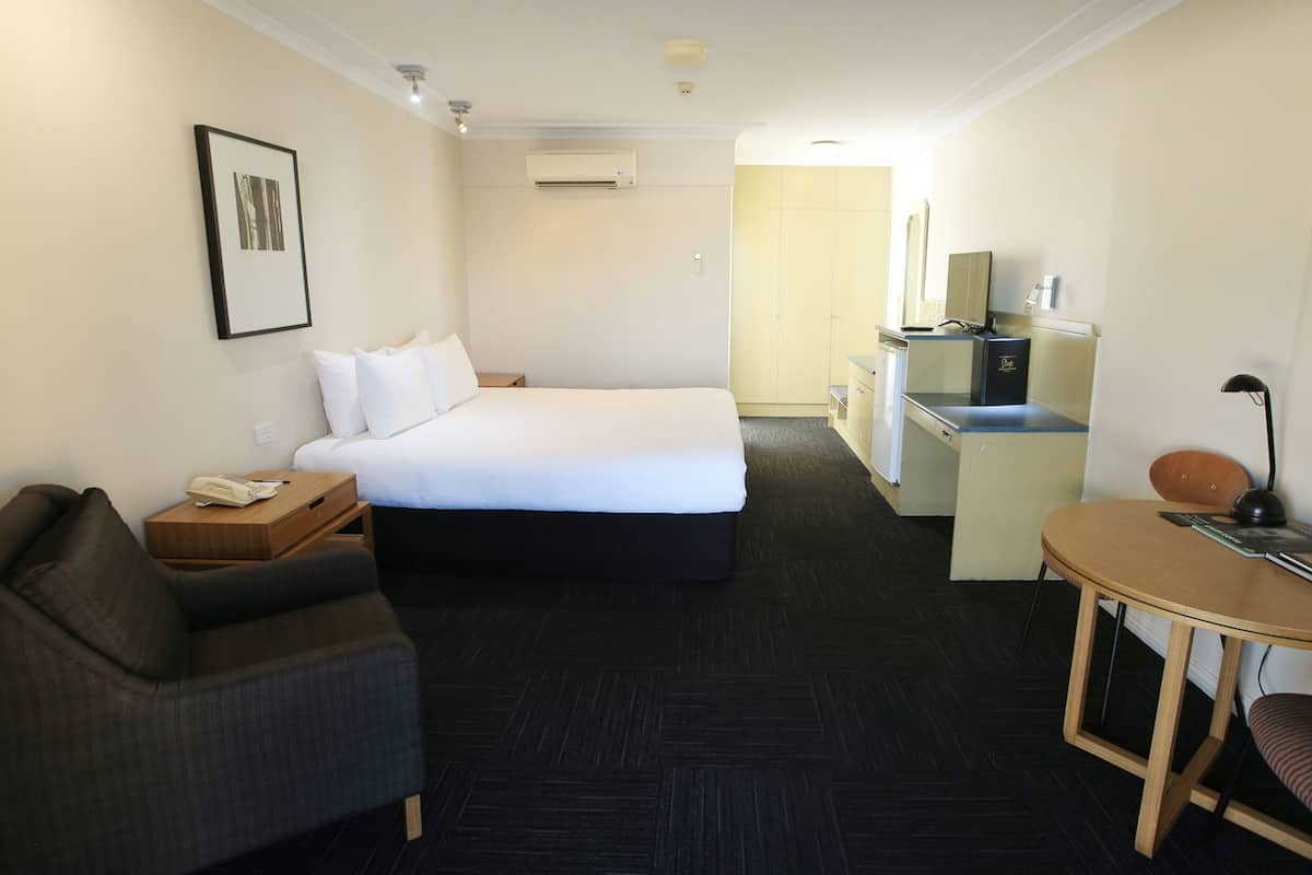 Habitación de hotel con cama, escritorio, silla, pequeño sofá, teléfono y equipo de aire acondicionado.