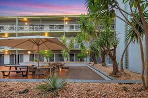 Un patio con mobiliario exterior, palmeras y un edificio con balcones.