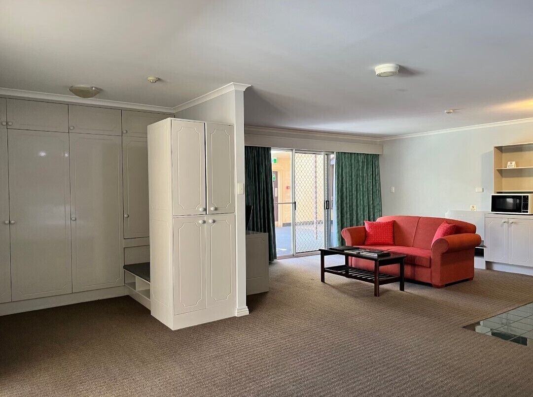 A compact living space with a kitchenette, a red sofa, and a sliding glass door leading to a balcony.