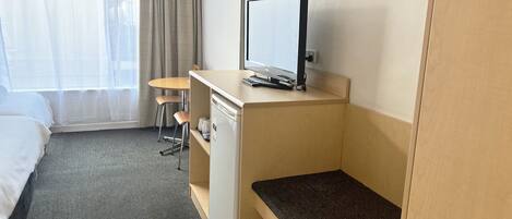 A hotel room with a bed, a desk with a computer, a chair, and a small table.