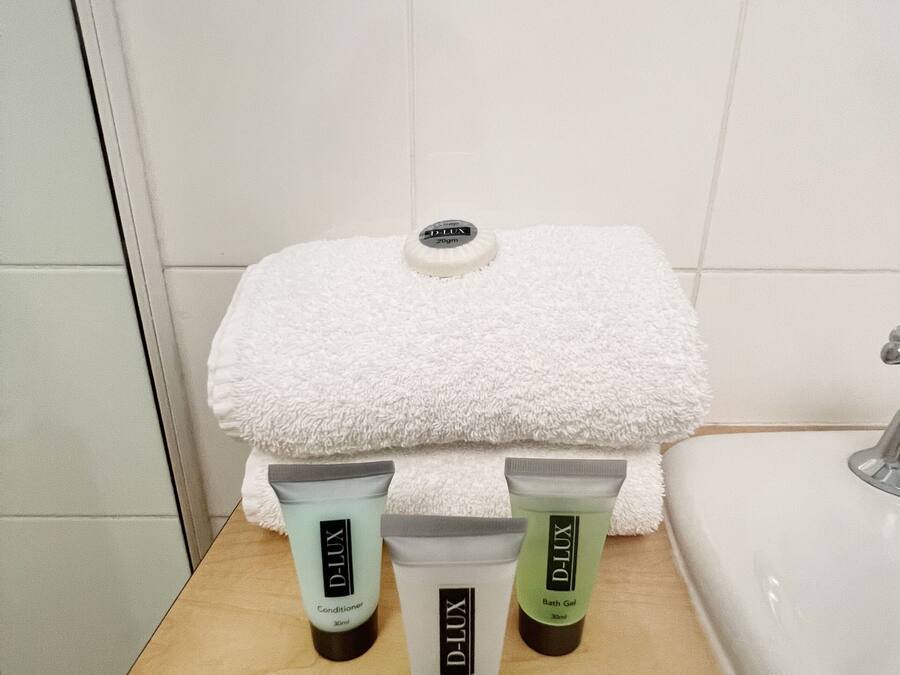 A bathroom with a white towel, a mirror, and three D-Lux toiletries on a wooden tray.
