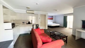 A compact hotel room with a kitchenette, a sofa, a bed, and a TV.