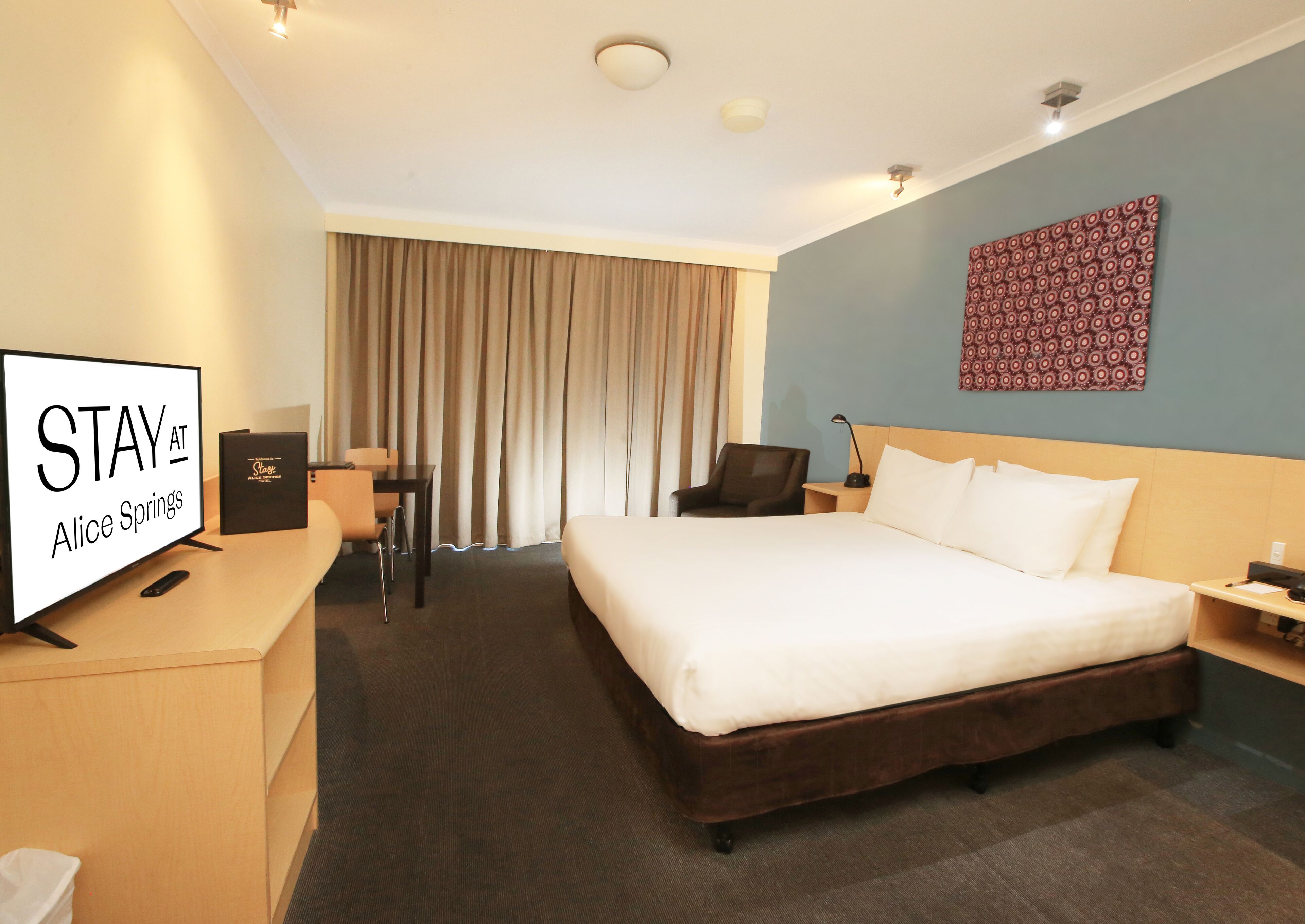 A hotel room with a bed, a desk, a chair, a TV, and a wall with a patterned design.