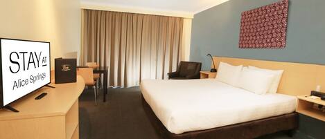 A hotel room with a bed, a desk, a chair, a TV, and a wall with a patterned design.
