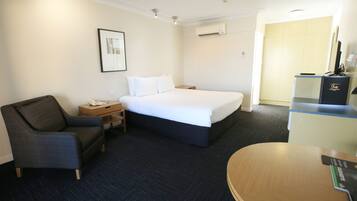 Una habitación de hotel con cama, una silla, un escritorio y un minibar.