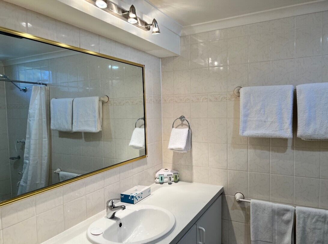 A bathroom with a large mirror, white sink, and two towel racks.