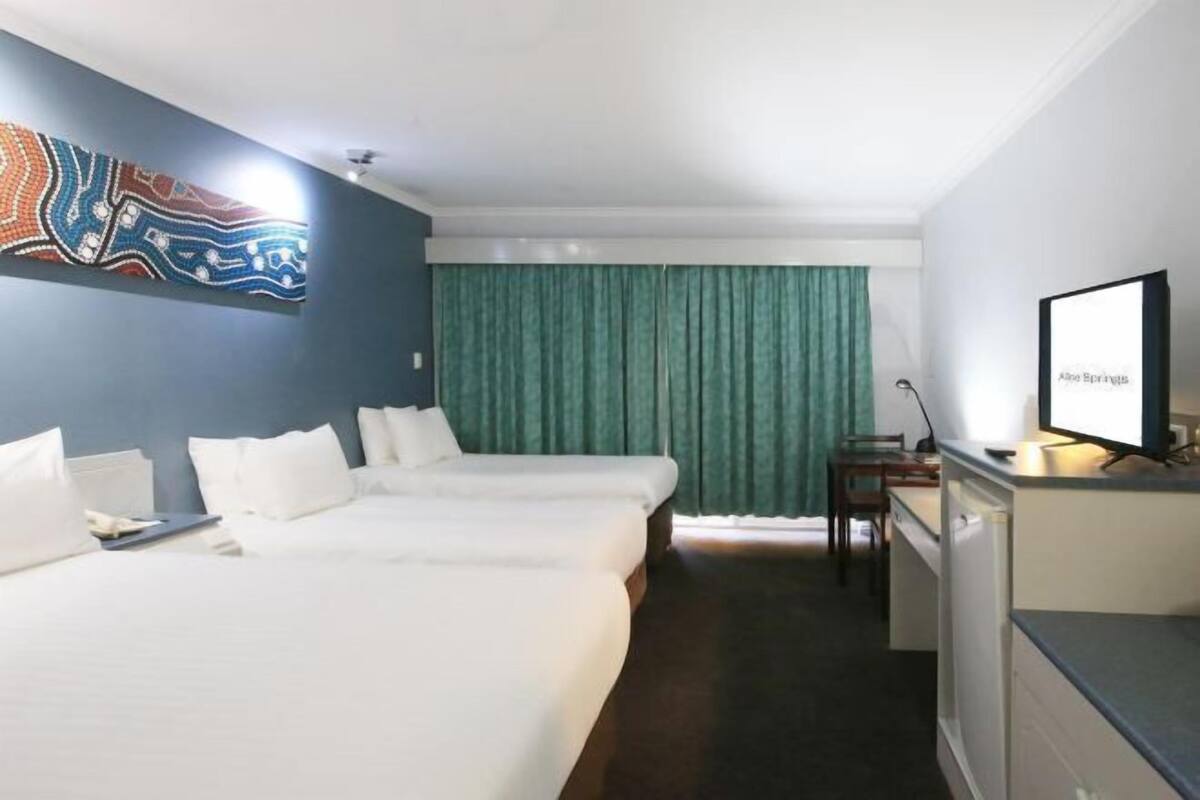 A hotel room with two beds, a desk, a television, and a green curtain.