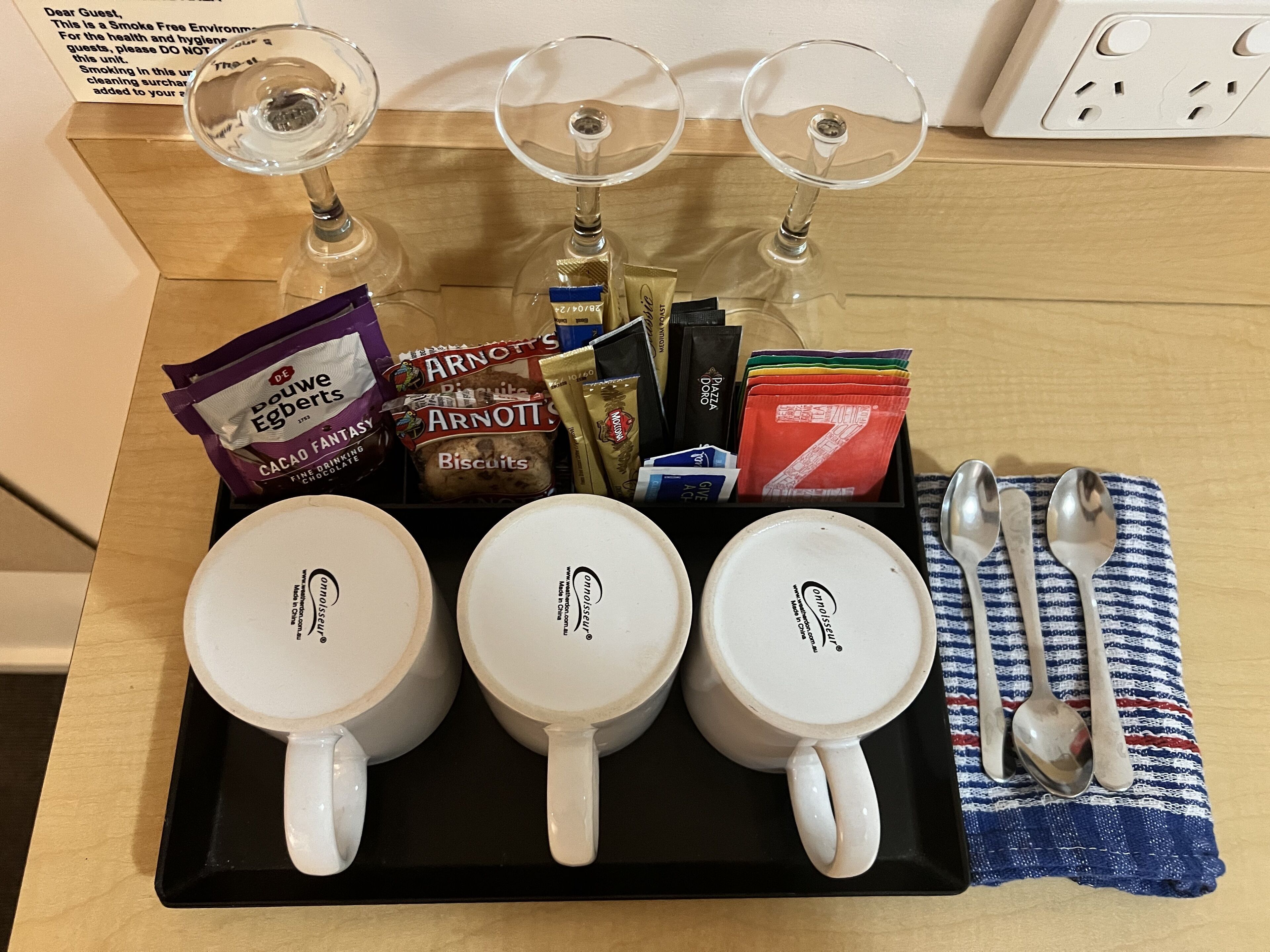 A tray with three white mugs, a set of silverware, and a variety of snacks and beverages.