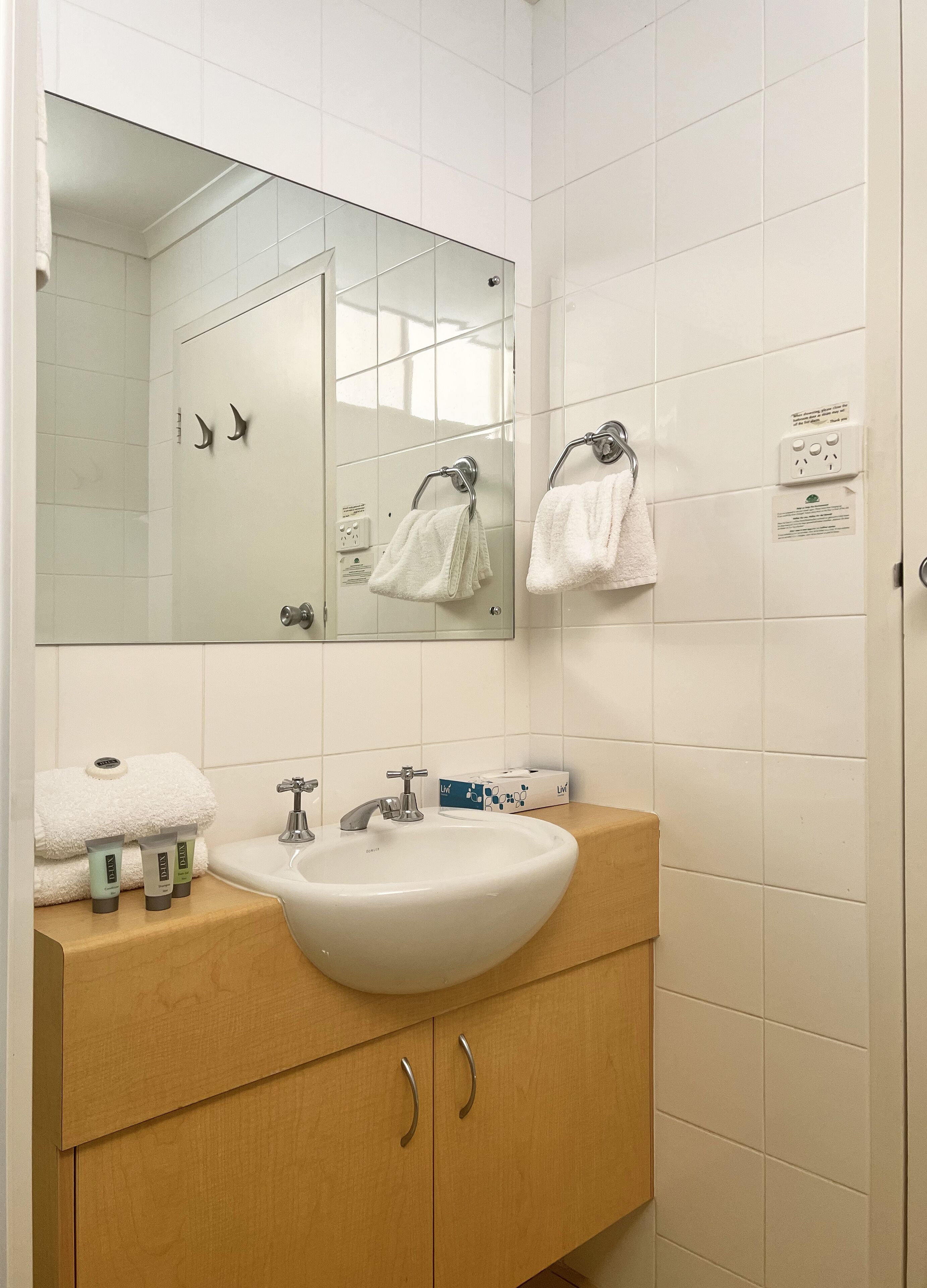 A bathroom with a white sink, mirror, and two towel racks. There are toiletries on the sink counter.