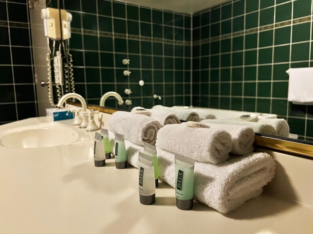 A bathroom with a sink, mirror, and green tiled walls. There are towels and toiletries on the counter.