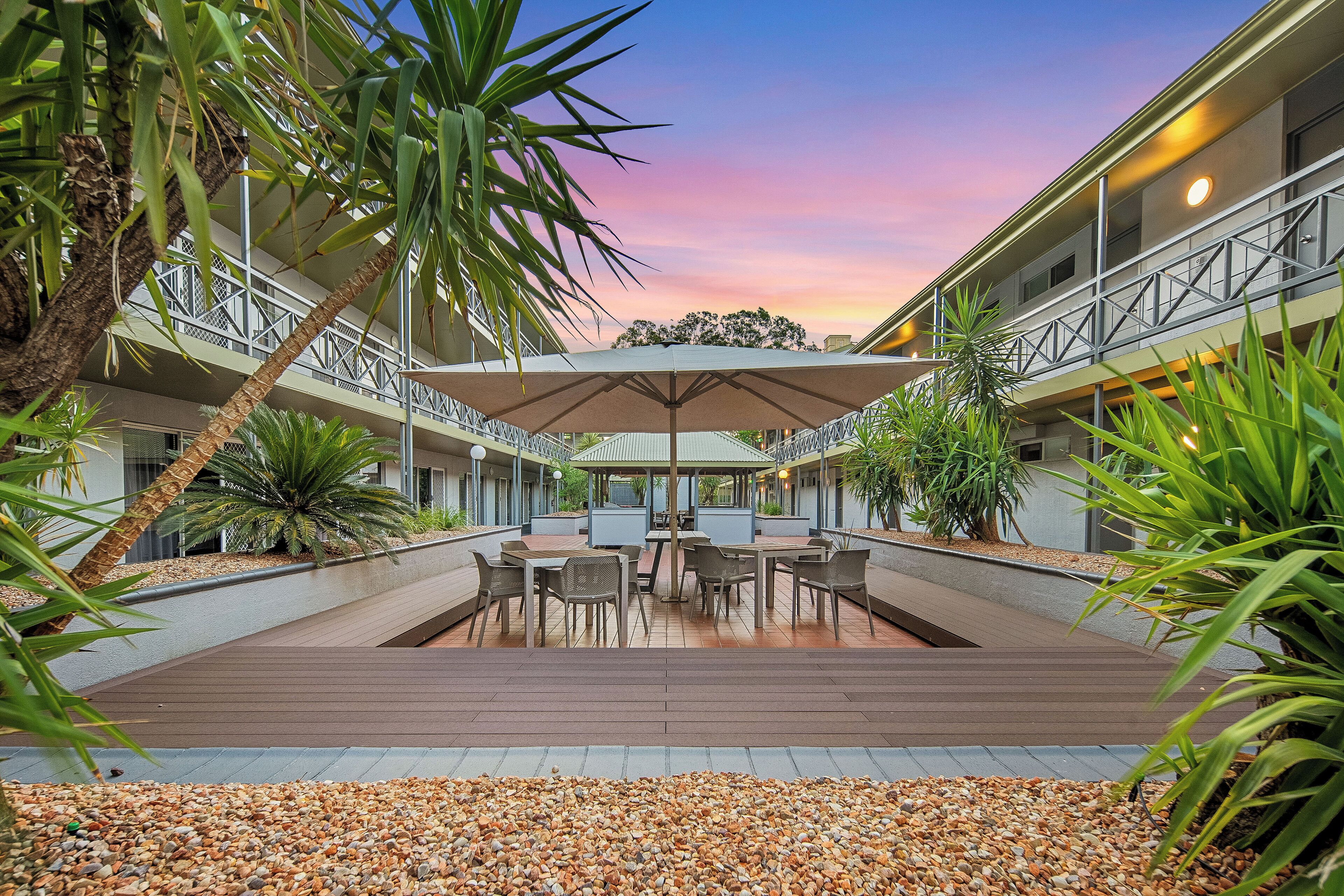 Un patio con mobiliario exterior, palmeras y vistas al atardecer.