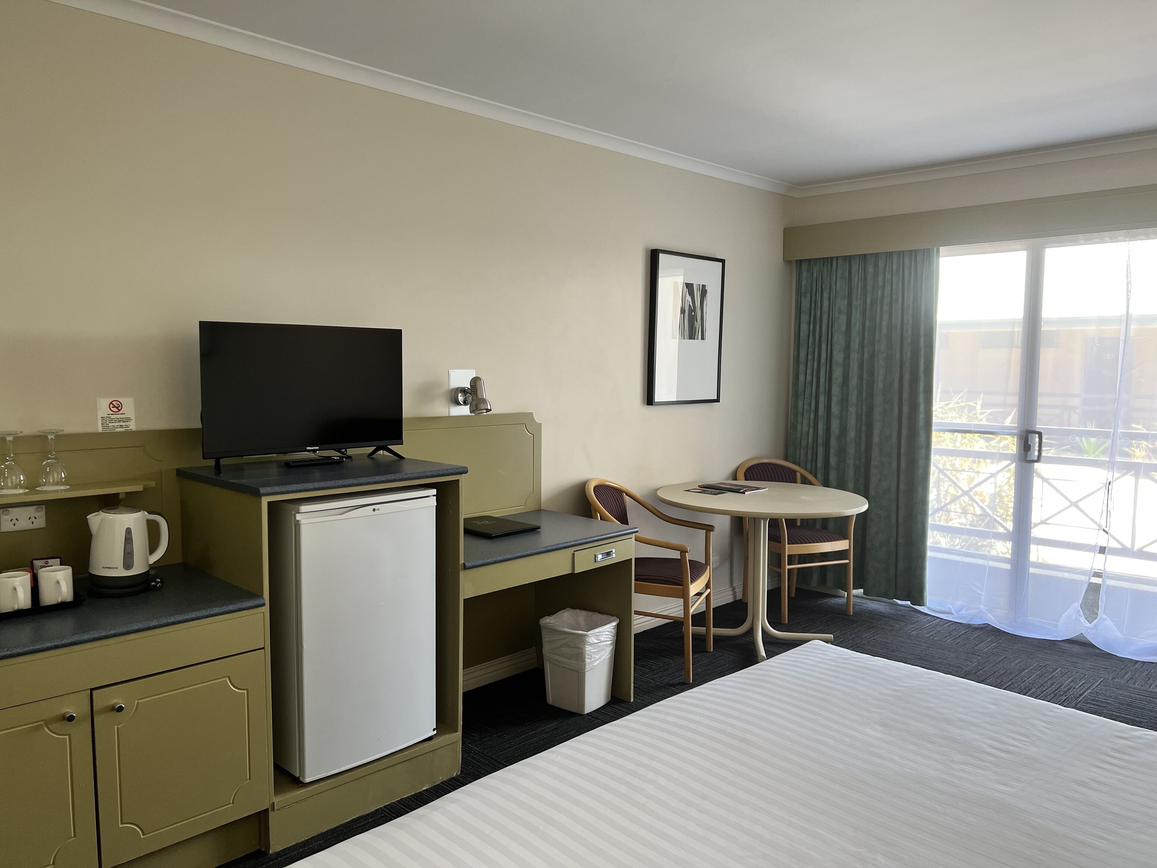 A hotel room with a bed, a desk with a computer, a television, a coffee maker, and a small table with chairs.