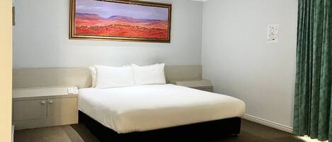 A hotel room with a large bed, a nightstand, a wall-mounted painting, and a green curtain.