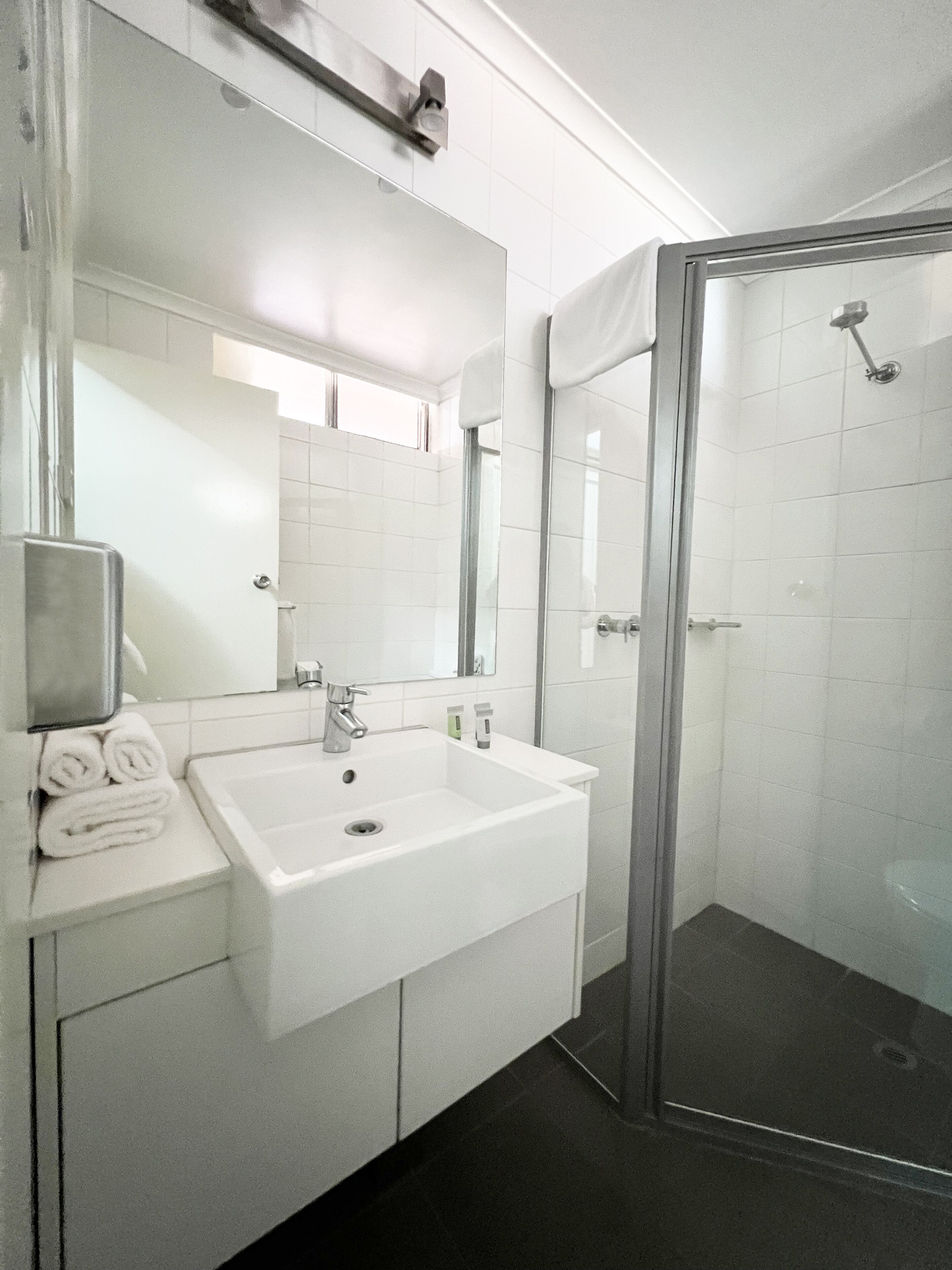 Un baño con lavamanos blanco, espejo y cabina de ducha de vidrio.