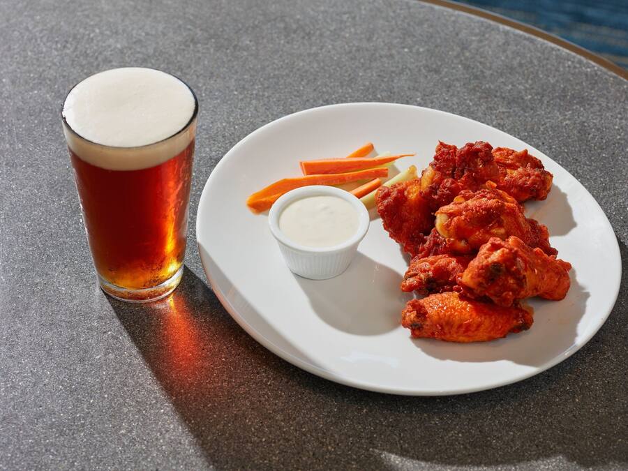 Prato de frango frito acompanhado de batatas rústicas e uma pequena tigela de molho, ao lado de um copo de cerveja sobre uma mesa.