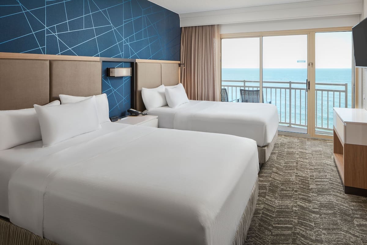 A hotel room with two beds, a desk, and a view of the ocean.