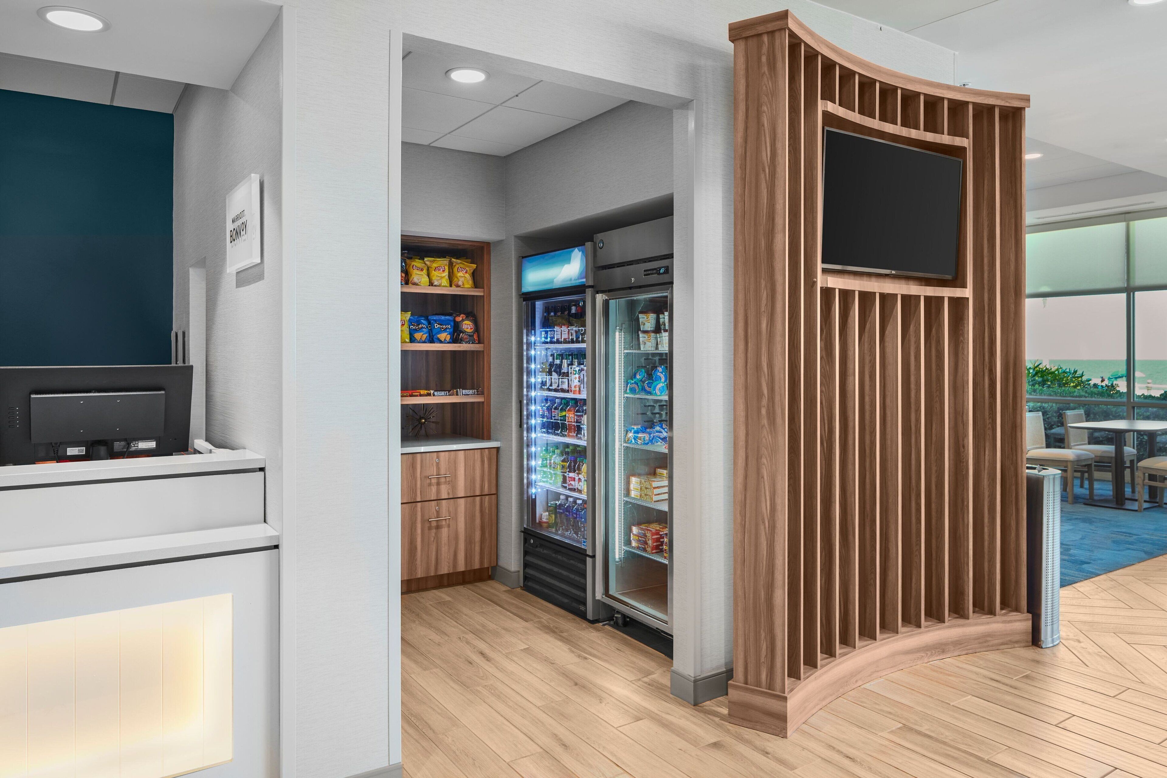 Uma área de recepção moderna com uma TV de tela plana, um refrigerador cheio de lanches e um divisória de madeira.
