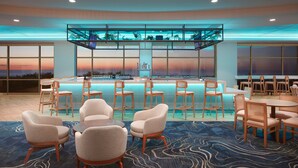A modern hotel lobby with a pool area, seating arrangements, and large windows offering a view of the sunset.