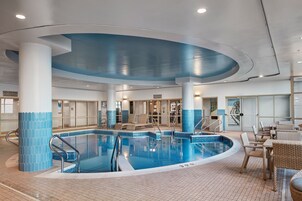 Uma piscina interior com áreas de beira-piscina espaçosas, espreguiçadeiras e chão revestido de azulejos.