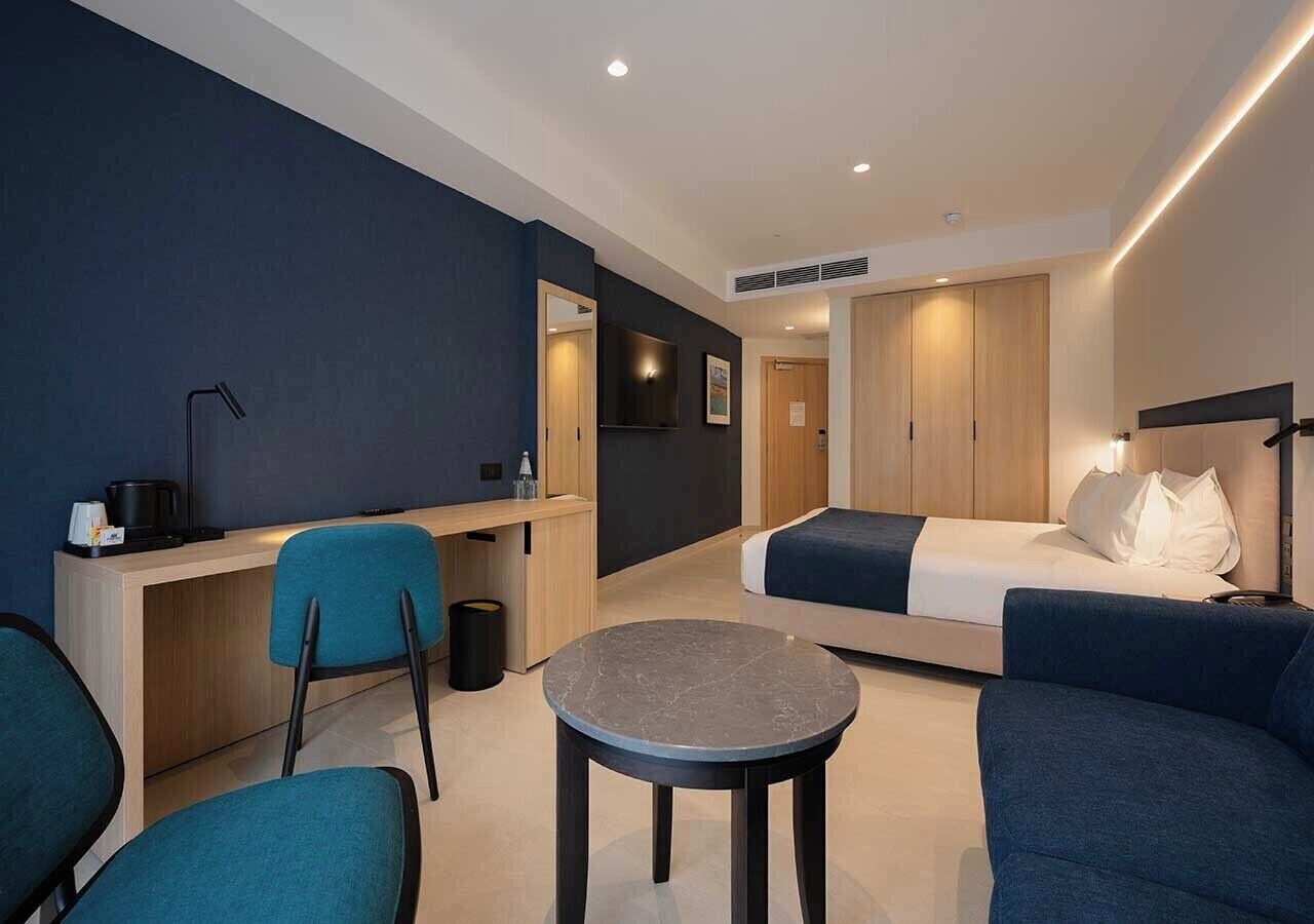A modern hotel room with a bed, a desk, a chair, and a small round table.