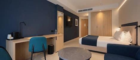 A modern hotel room with a bed, a desk, a chair, and a small round table.