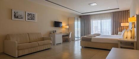 A modern hotel room with a sofa, a bed, a desk, and a TV.