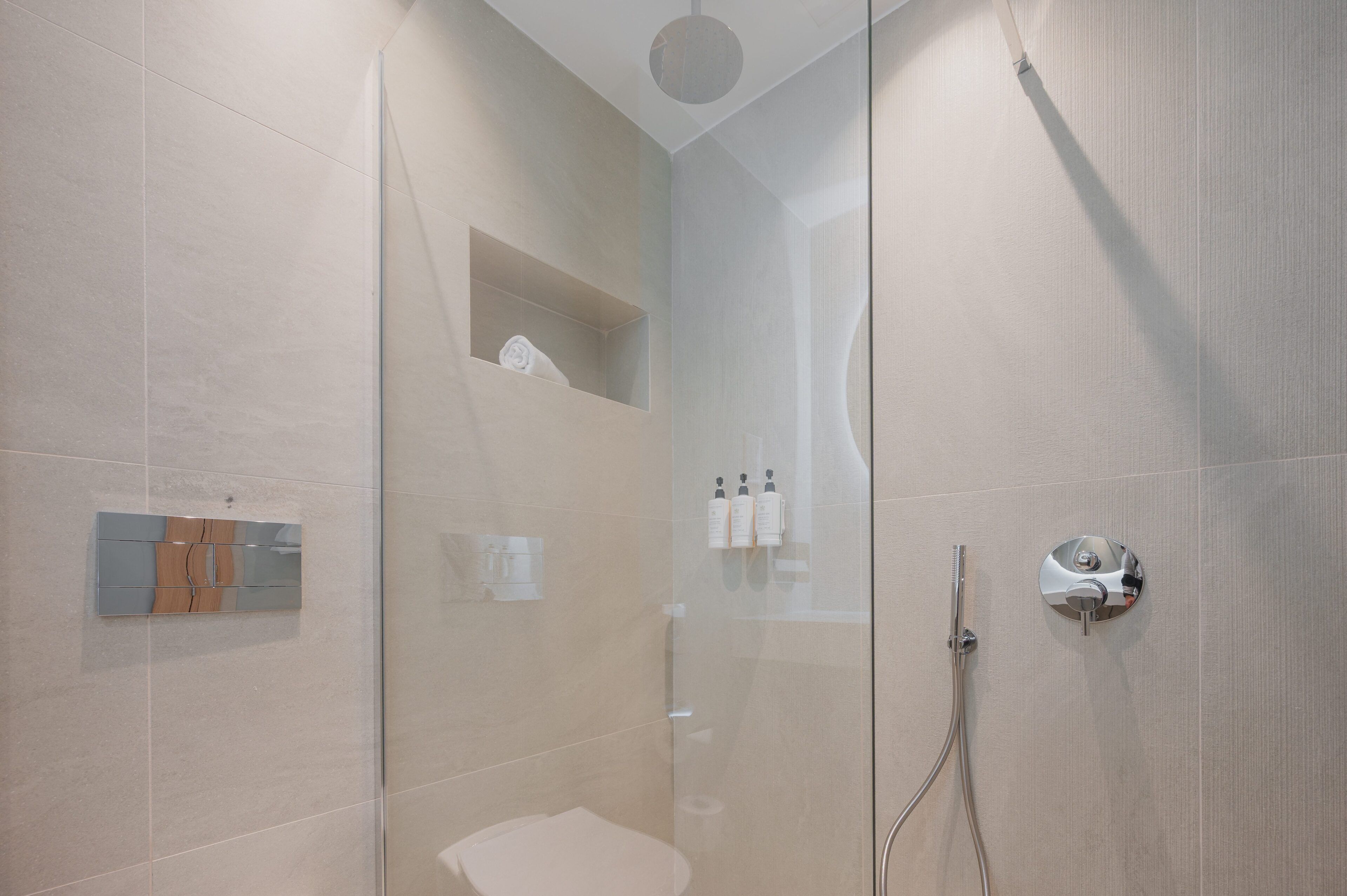 Une salle de bain moderne avec une douche à parois de verre, des toilettes et une étagère contenant des articles de toilette.