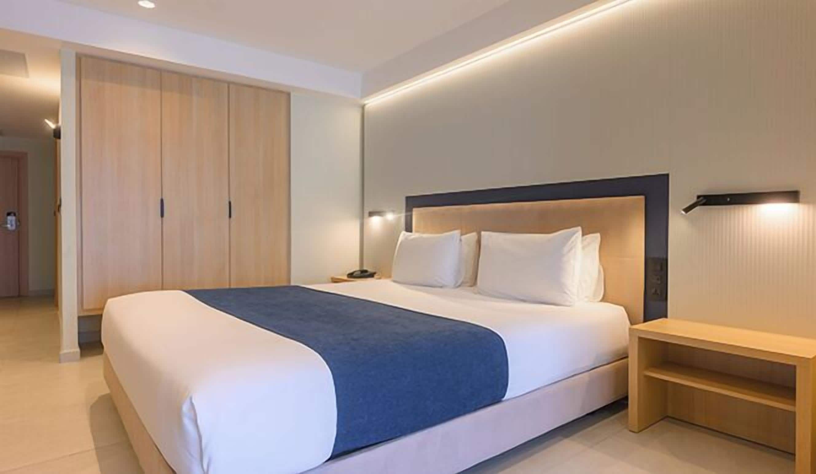 Una habitación de hotel moderna con una cama grande, un armario de madera y una mesita de noche.