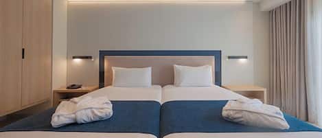 A hotel room with two beds, a wooden wardrobe, bedside lamps, and a window with curtains.