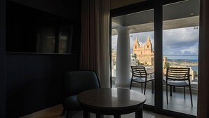 A room with a balcony, two chairs, a table, and a view of a historic building.