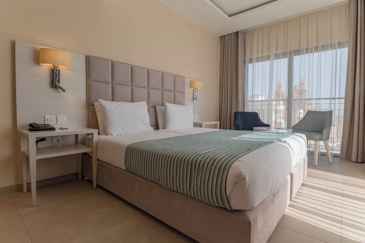 Habitación de hotel moderna con una cama grande, un escritorio, una silla y vistas a la ciudad.
