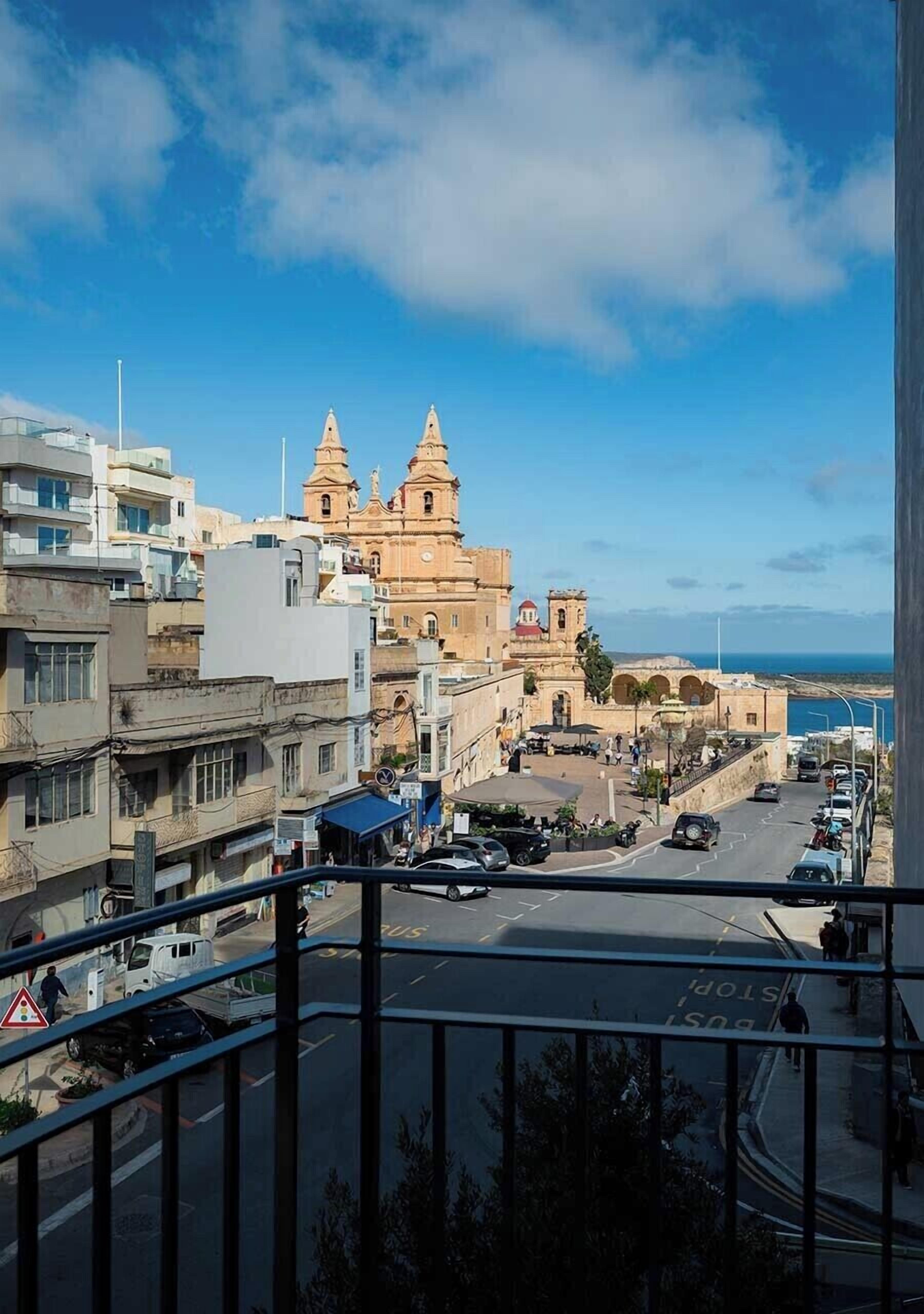 Paisatge urbà costaner amb un edifici històric destacat que presenta dues torres, edificis moderns i un cel blau clar.